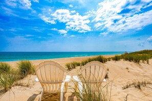 Two beach chairs facing a sandy beach with a clear sky and ocean view.