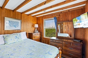 Ein Schlafzimmer mit Holzwandverkleidung, einem Bett, einer Kommode und einem Fenster mit Blick auf Grünflächen.