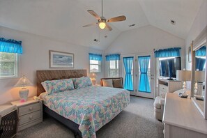 Een slaapkamer met een bed, nachtkastje, dressoir, plafondventilator en televisie.