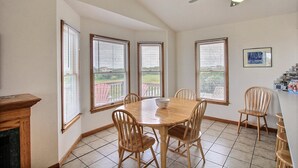 Ein Esszimmer mit Holztisch und -stühlen, großen Fenstern mit Jalousien, einem Deckenventilator und Blick ins Freie.