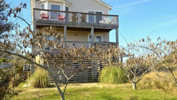 Ein zweistöckiges Haus mit einem Balkon im oberen Geschoss, umgeben von trockener Vegetation.