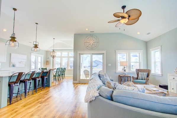 A spacious living area with a large sofa, a dining table with chairs, and a ceiling fan.