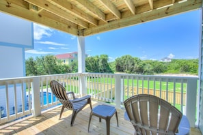 A covered deck with two chairs and a table, overlooking a swimming pool and a grassy yard with a wooden fence.