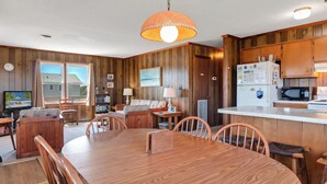Una habitación con paneles de madera, una mesa de comedor, sillas, un sofá, un televisor y una zona de cocina con refrigerador y microondas.