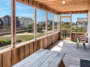 A covered outdoor deck with wooden benches and large windows offering views of neighboring houses and greenery. - Ten Forward: 500ft to Beach, Ocean Views OBX (Kitty Hawk)