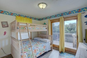 A room with a bunk bed, a window with curtains, a small desk, and a view of the outdoors.