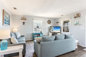 Relax in a spacious living room with a comfortable sofa, armchair, and large TV, surrounded by nautical-themed decor and a bookshelf.