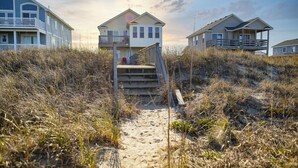 A pathway leading to a beach house with a wooden staircase, surrounded by tall grasses and sand. - 5060 Dolphin's Watch * Oceanfront * Elevator (Kill Devil Hills)