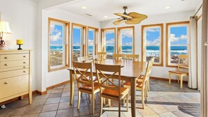 A dining area with a view of the ocean, a ceiling fan, and a wooden table with chairs. - 5060 Dolphin's Watch * Oceanfront * Elevator (Kill Devil Hills)