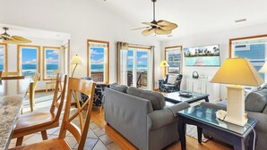 A spacious living area with a view of the ocean, a ceiling fan, and a television on the wall. - 5060 Dolphin's Watch * Oceanfront * Elevator (Kill Devil Hills)