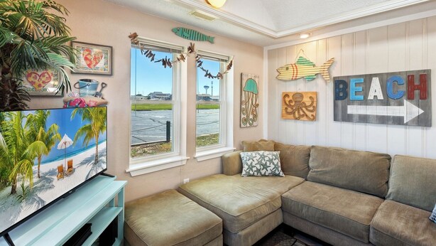 A beach-themed living room with a large window, a TV, and a couch. - Flip Flop Inn * No Stairs * Close to Beach (Kill Devil Hills)