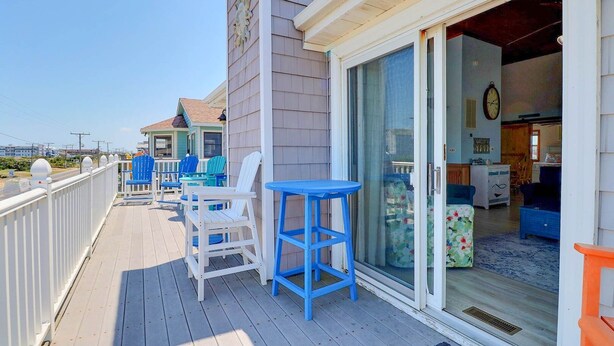 A wooden deck with outdoor seating, a glass door entrance, and a view of the ocean.