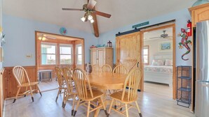 A spacious kitchen with a wooden dining table and chairs, a ceiling fan, and a view into the adjacent bedroom.