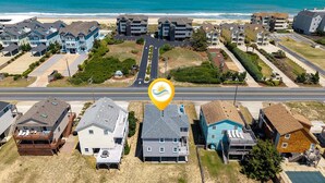 A coastal residential area with houses, a road, and a beach in the background.