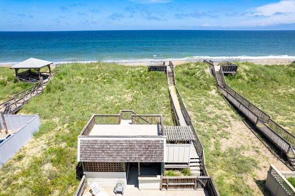 A beach house with a wooden deck, a small covered area, and a view of the ocean.