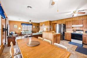 A compact kitchen with wooden cabinets, a refrigerator, stove, and a dining area with a wooden table and chairs.