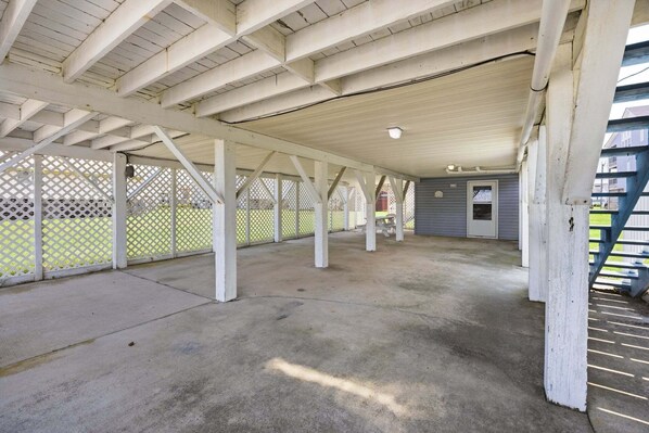 Un espace extérieur couvert et vide, doté d’un sol en béton et de poutres en bois peintes en blanc.