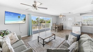 A spacious living room with a large window, a ceiling fan, and a dining area. - Cozy Beach Villas, Huge Shared Pool, Walk to Beach, Times Square Restaurants! (Fort Myers Beach)