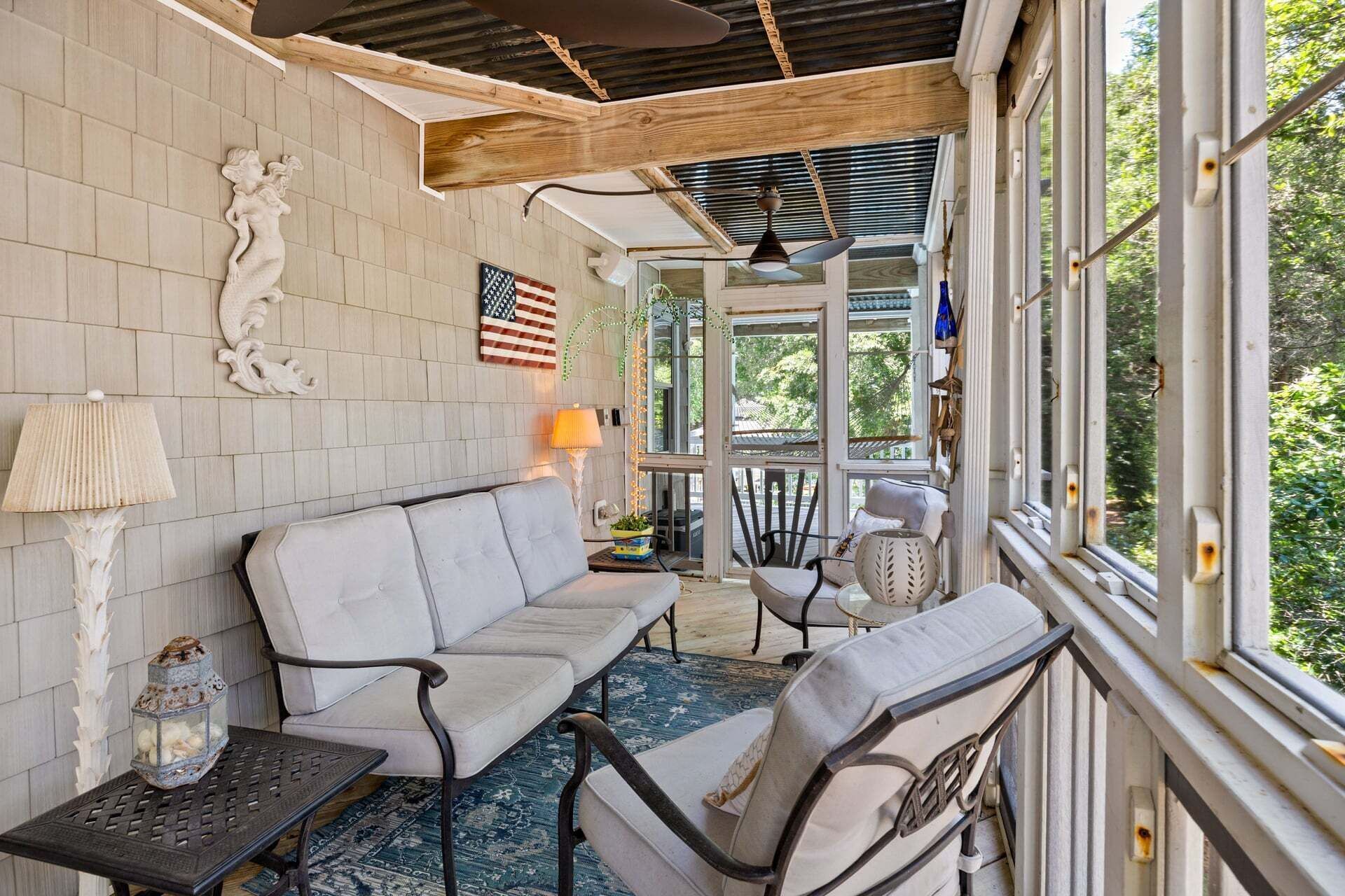 A sunlit room with a sofa, chairs, a table, and a view through large windows.