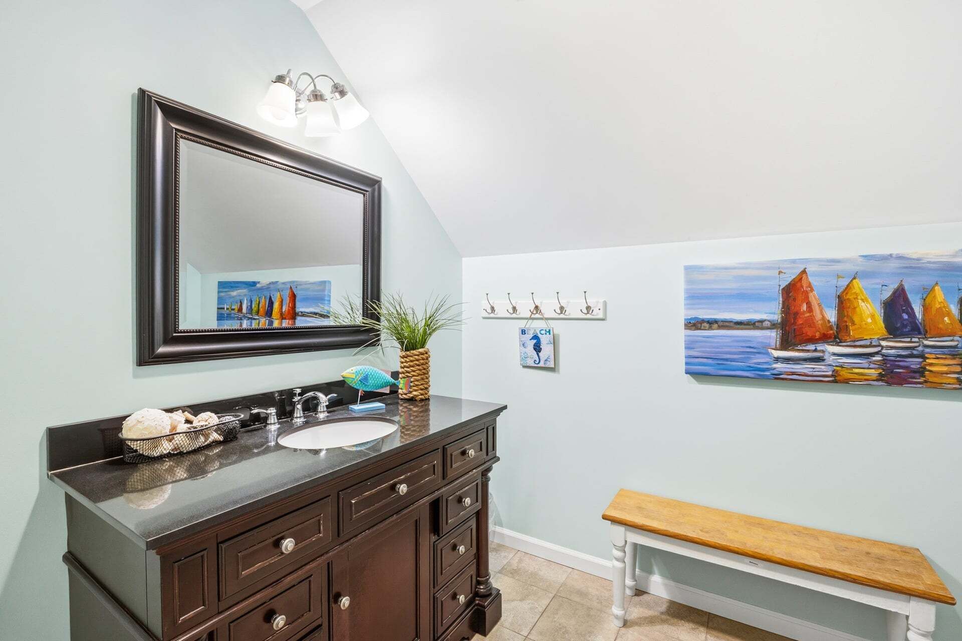 A bathroom with a dark wooden vanity, a mirror, a sink, and a bench.