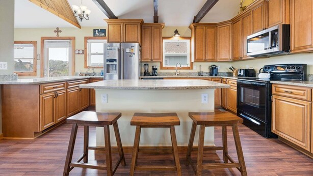 Une cuisine avec des meubles en bois, un grand îlot central doté de tabourets, un réfrigérateur, une cuisinière et un four à micro-ondes.