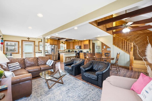 A spacious living area with leather sofas, a glass coffee table, and a kitchen in the background.
