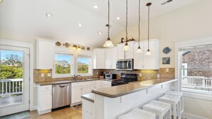 Una cucina moderna con mobili bianchi, una grande isola con sgabelli da bar, elettrodomestici in acciaio inossidabile e illuminazione a sospensione.