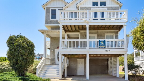 Una casa sulla spiaggia su due piani, con un balcone, un garage e un cartello pubblicitario per affitti vacanze.
