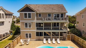 A multi-story building with a swimming pool, outdoor seating, and a wooden deck. - Ferrari II *SEMI-OCEANFRONT*Pool*HotTub*ArcadeGame (Nags Head)