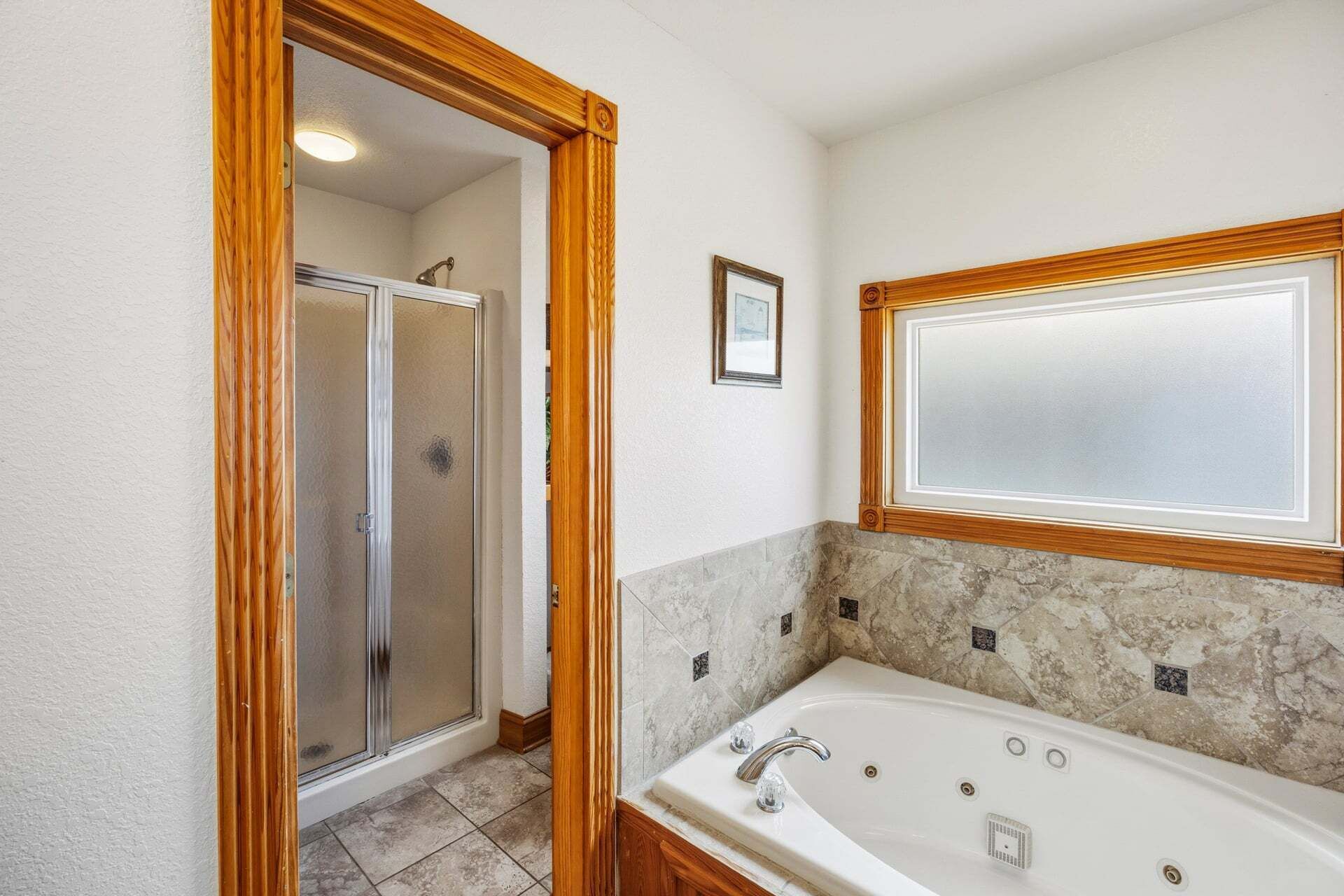 A bathroom with a large bathtub, a shower, and a wooden-framed mirror.