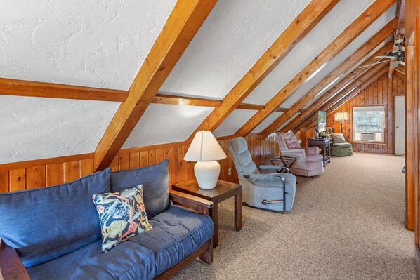 A cozy attic bedroom with wooden beams, a blue sofa, and two armchairs. - 6137 Harper * Oceanfront (Nags Head)