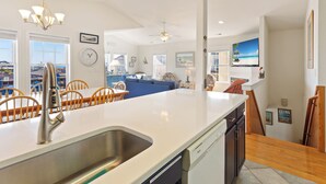 Une cuisine moderne dotée d’un grand îlot central, un coin repas avec des chaises en bois et un salon avec un canapé bleu.