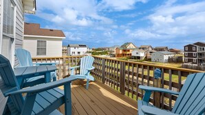 Une terrasse en bois avec des chaises bleues, une balustrade en bois et une vue sur des immeubles d’habitation.