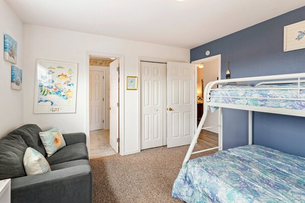 A bedroom with a bunk bed, a sofa, and a door leading to another room. - Poolside Paradise*2 min to Beach*Dogs*Pool (Nags Head)