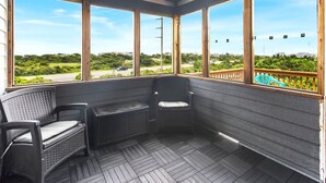 A covered porch with two wicker chairs and a bench, large windows offering a view of a road and greenery. - Poolside Paradise*2 min to Beach*Dogs*Pool (Nags Head)