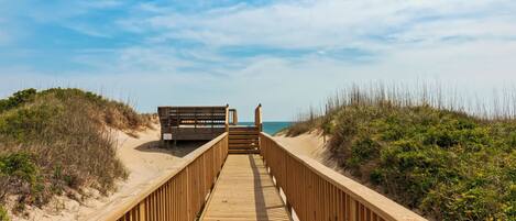 A wooden boardwalk leading to a beach with a bench and a small structure.