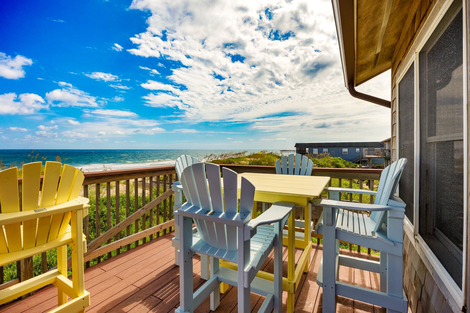 A deck with a table and chairs, overlooking a beach and ocean.