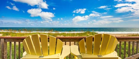 Two yellow chairs facing a beach with a wooden deck and a wooden railing.