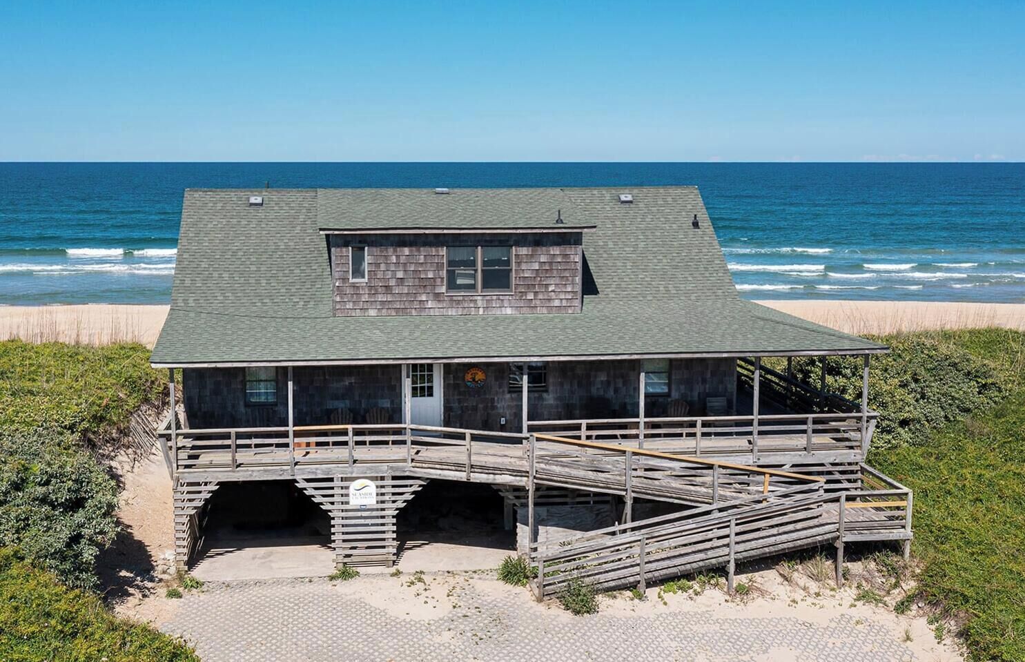 A wooden beach house with a balcony, a covered area, and a staircase leading to the entrance.