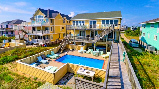 Um hotel na praia com piscina, várias varandas e um deque de madeira.