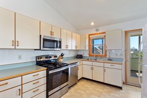 A modern kitchen with white cabinets, a stainless steel stove, a microwave, and a window with a view of the outside.