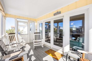 Ett takförsett utomhusområde med ett trädäck, vita räcken och utsikt över stranden.