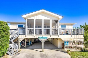 Une maison de vacances située sur la plage, dotée d’un porche couvert, d’un escalier et d’une enseigne indiquant « Séjours au bord de la mer ».