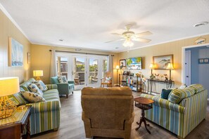 A living room with striped sofas, a wooden armchair, a ceiling fan, and a door leading outside.