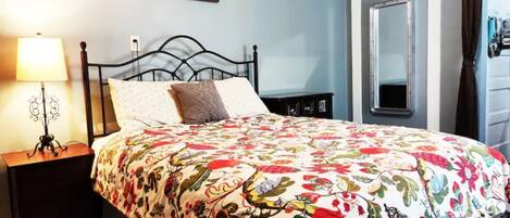 A bedroom with a floral bedspread, a bedside lamp, a mirror, and a sign on the wall.