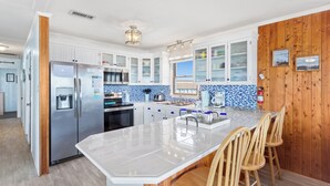 A modern kitchen with white cabinets, a stainless steel refrigerator, a built-in oven, and a large island with bar stools.