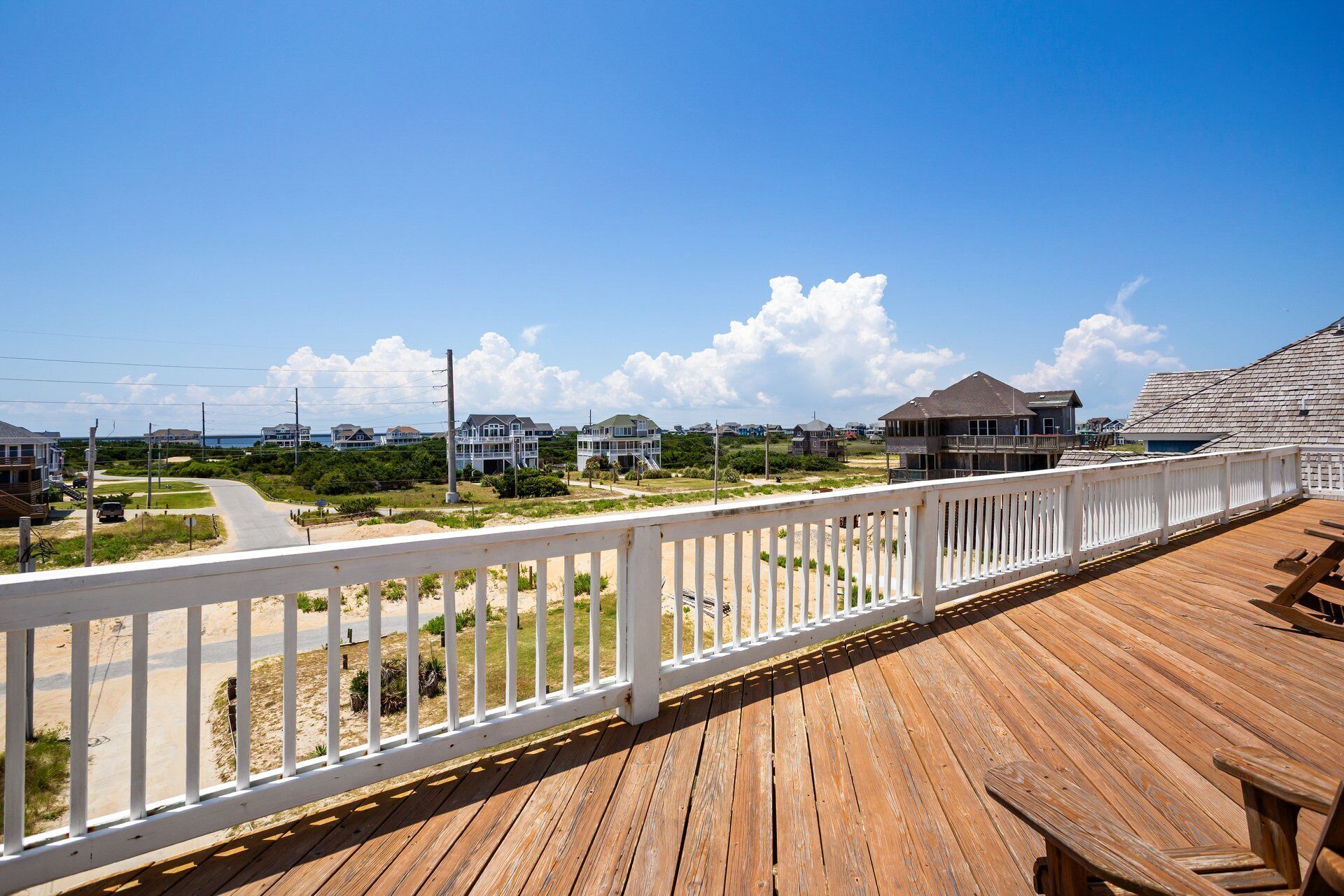 A wooden deck with a white railing overlooking a beach and houses.