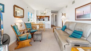 Ein Wohnzimmer mit einer Couch, Sesseln, einem Couchtisch und einer Küche im Hintergrund.