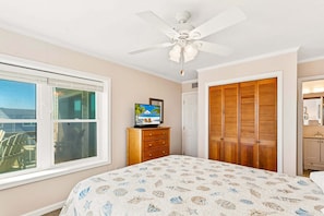 A bedroom with a bed, a ceiling fan, a TV on a dresser, and a wooden closet.