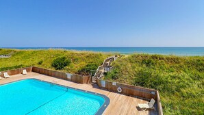 Eine Holzterrasse mit Pool, Liegestühlen und einer Treppe zum Strand.